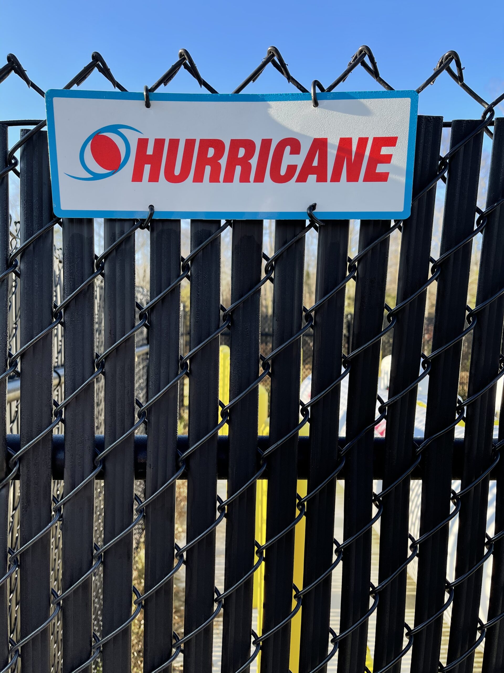 Black galvanized chain link fencing including vertical privacy slats with a Hurricane Fence Company sign attached.